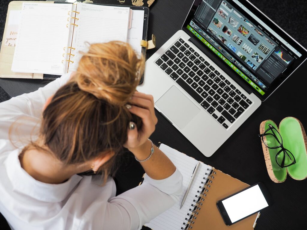 pexels photo 313690 Overhead view of a stressed woman working at a desk with a laptop, phone, and notebooks.